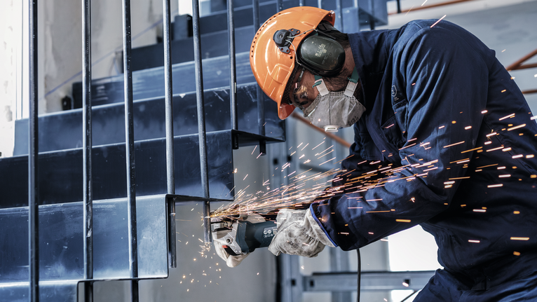 佩戴安全设备的人员使用角磨机研磨金属楼梯，产生火花。.