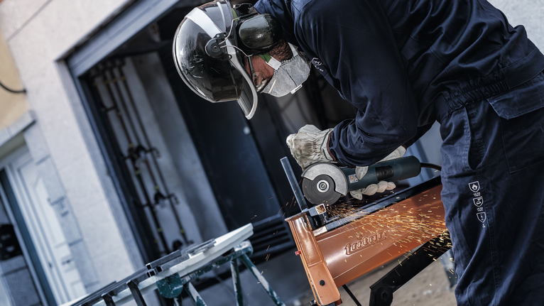 一名佩戴安全设备的人使用角磨机切割金属，产生火花。