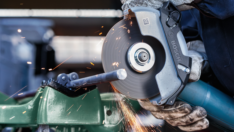 佩戴安全设备的人用圆锯切割金属棒，产生火花。