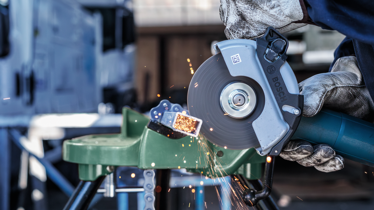 一名佩戴安全设备的人用电磨切割金属，火花四溅。