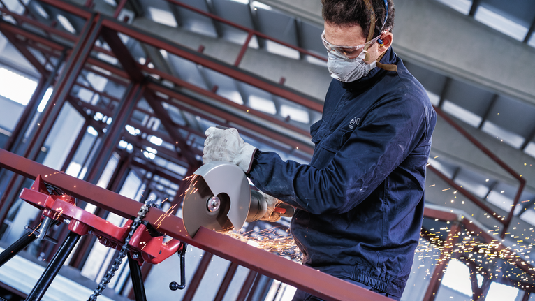 一名佩戴安全设备的人使用角磨机切割金属，产生火花。