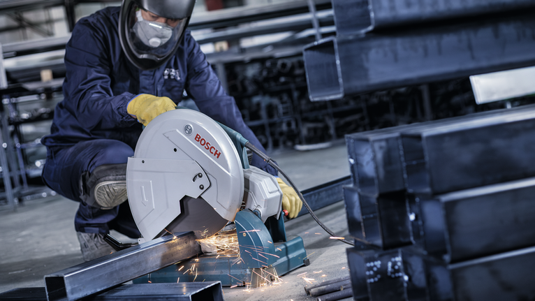 佩戴安全设备的人用锯子切割金属梁，产生火花。.