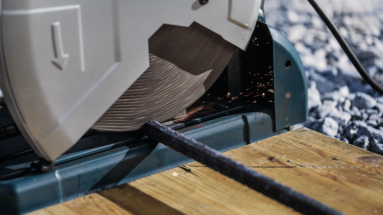 金属切割锯在木质工作台面上切割钢棒。