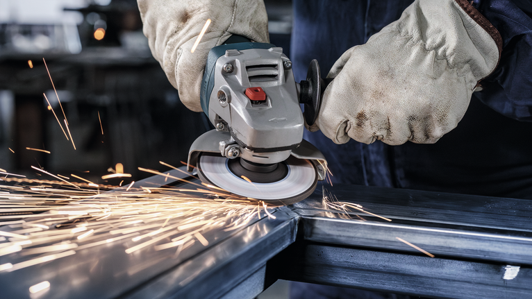 工人穿着安全装备打磨钢梁，产生火花。.