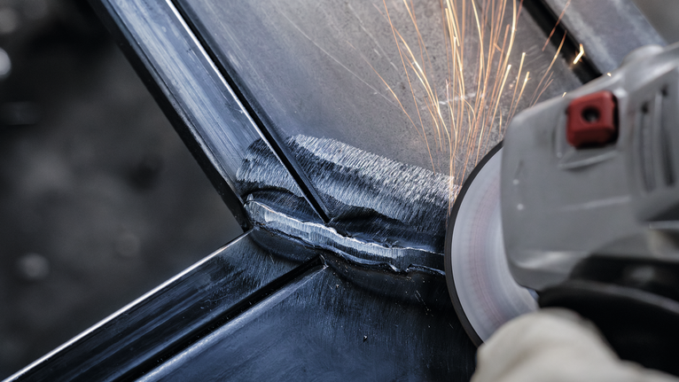 一名戴着手套的工人正在打磨金属接头，产生火花。.