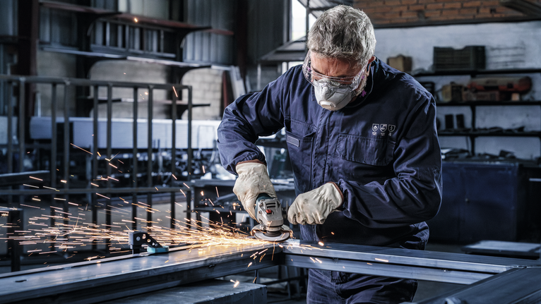 一名戴着安全设备的工人在车间研磨金属，产生火花。.