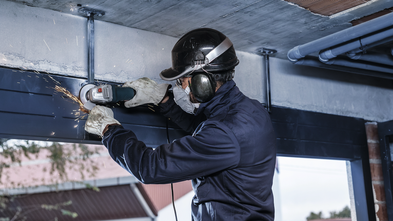 一名佩戴安全设备的人正在磨削钢梁，产生火花。