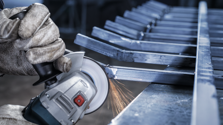 一名佩戴安全设备的人正在研磨金属梁，产生火花。