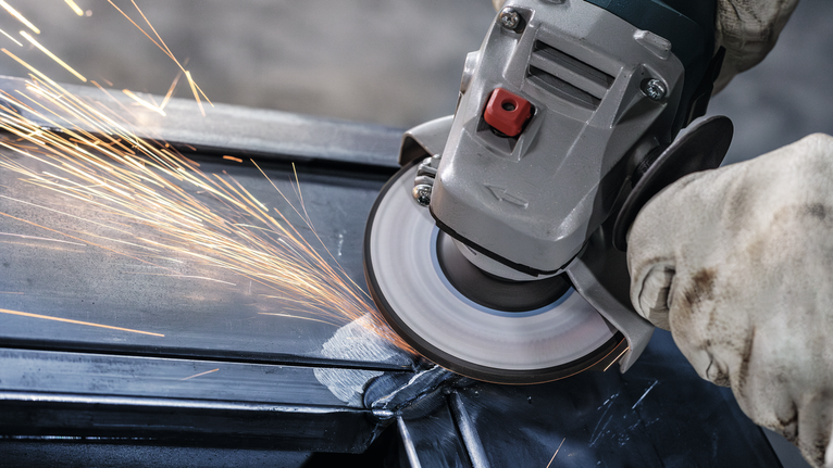 佩戴安全设备的人研磨金属，产生火花。