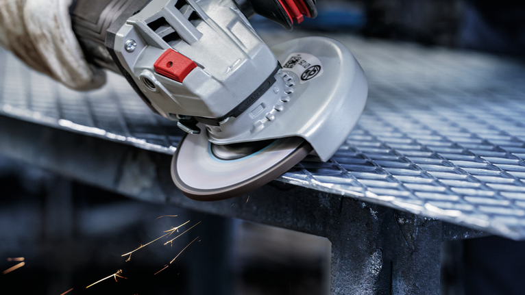 佩戴安全设备的人员使用手持工具研磨金属格栅。