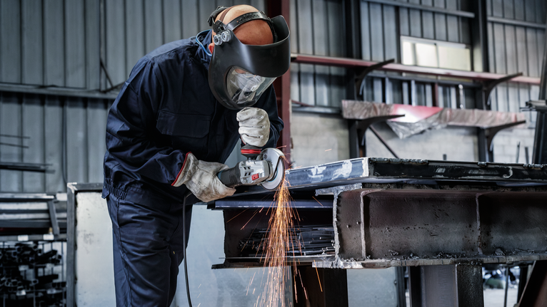 佩戴安全设备的人研磨金属，产生飞溅的火花。