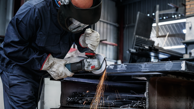 一名佩戴安全设备的人员在车间研磨金属，产生火花。