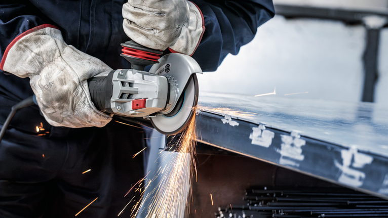 一名佩戴安全设备的人员使用电动工具打磨金属板的边缘。