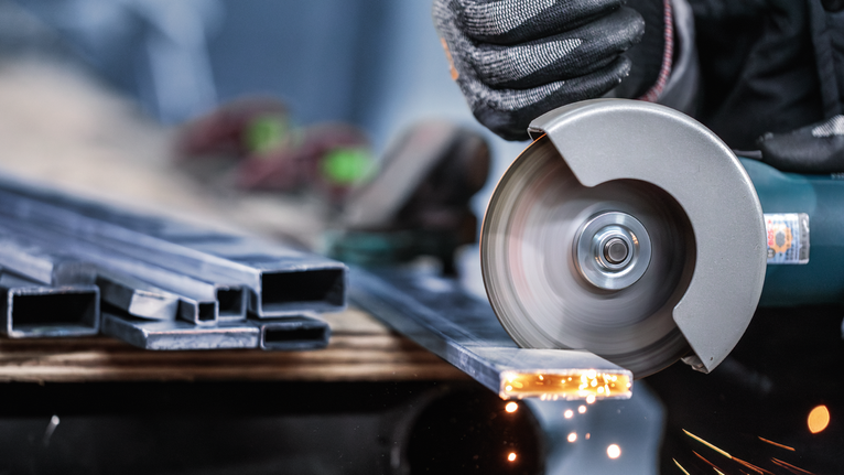 一名佩戴安全设备的人员正在使用角磨机切割金属型材。