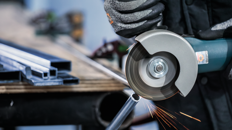 佩戴安全设备的人员使用角磨机切割金属管。