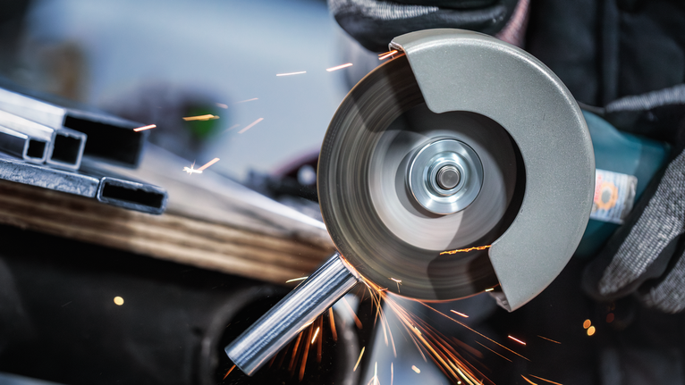 佩戴安全设备的人员使用角磨机切割金属管道。