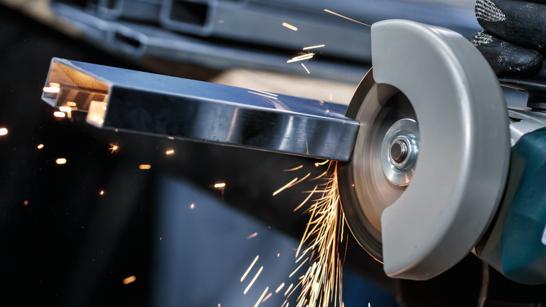 佩戴安全设备的人员使用手持切割工具研磨金属棒。