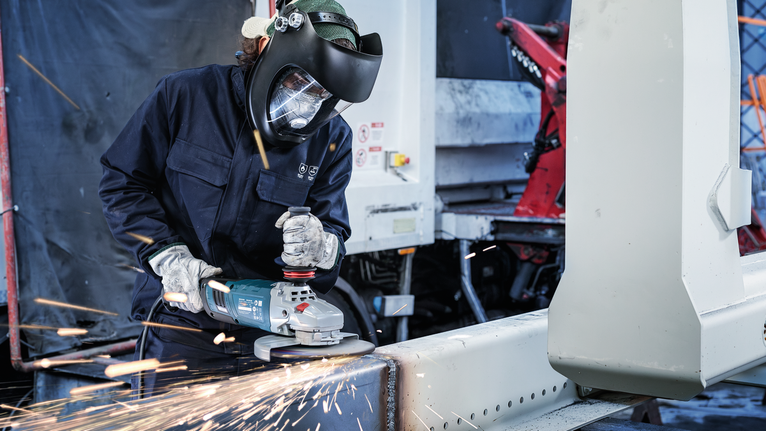 一名佩戴安全设备的人员使用角磨机切割金属梁。