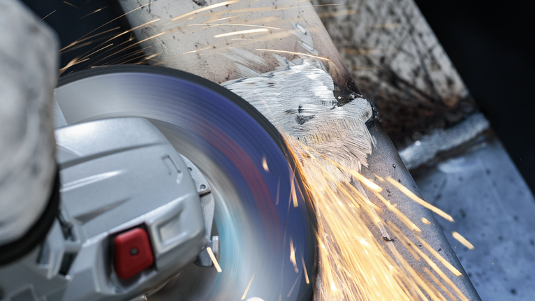 佩戴安全设备的人研磨金属表面，产生明亮的火花。