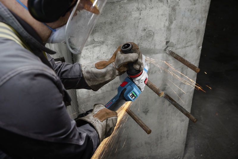 一名佩戴安全设备的人员正在研磨混凝土墙上裸露的钢筋。.