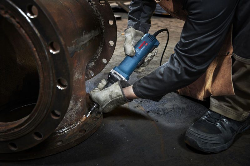 一名佩戴安全设备的人员使用直磨机对金属法兰进行打磨。.