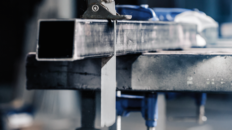 金属锯在工作台上切割钢制矩形管。