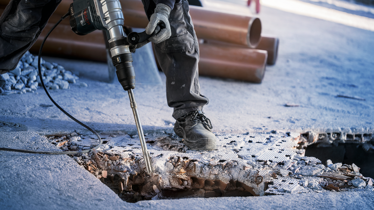 一名佩戴安全设备的人员用旋转锤破碎混凝土。