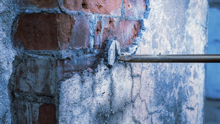 凿子钻入砖块和混凝土，穿透墙面。.