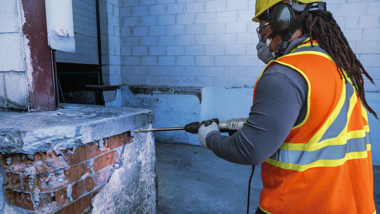 一名戴着安全设备的工人在建筑工地上钻入混凝土墙。.