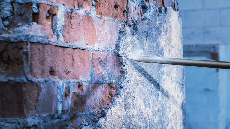 凿子从砖墙上除去混凝土灰泥。.