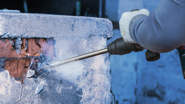 佩戴安全设备的人员使用拆除工具拆除混凝土墙。.