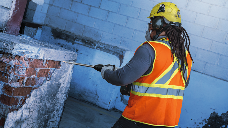 佩戴安全设备的人员使用拆除工具来破碎混凝土和砖块。.