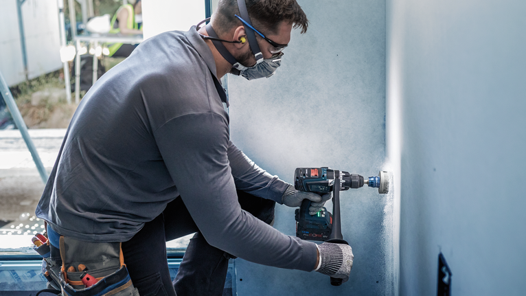 一名佩戴安全设备的人员在墙上钻了一个圆孔。