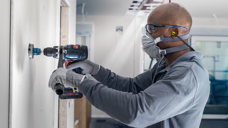 佩戴安全设备的人员在墙上钻一个圆孔。