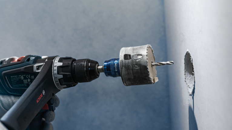 佩戴安全设备的人员用孔锯在墙上钻一个圆孔。