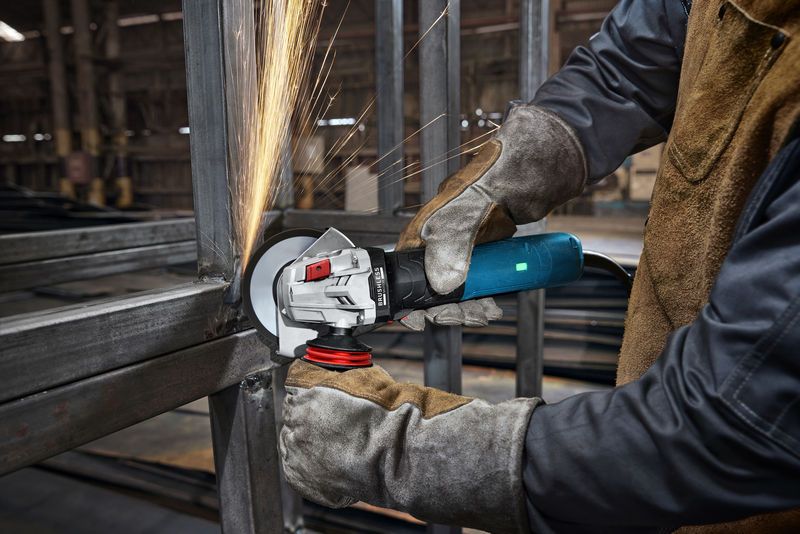 一名佩戴安全设备的人员在工业环境中研磨金属，产生火花。.