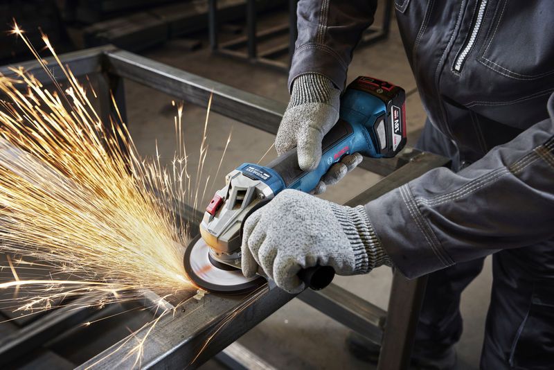 一名佩戴安全设备的人员正在使用角磨机打磨金属梁。.