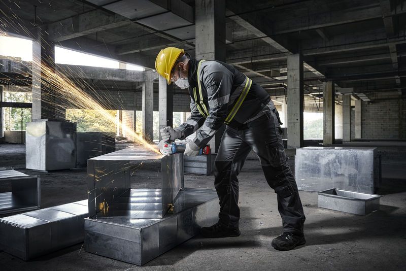 一名佩戴安全设备的人员在建筑工地上使用角磨机打磨金属管道。.