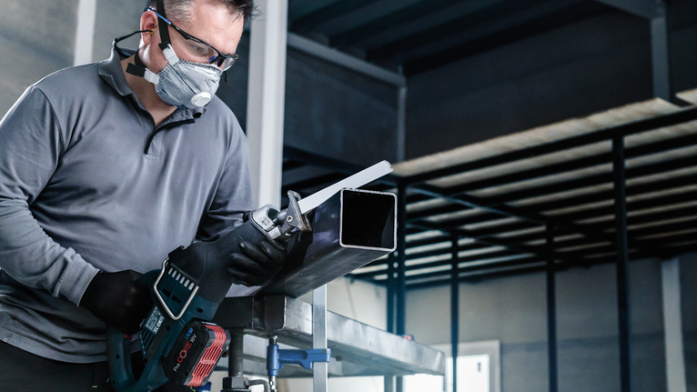 一名佩戴安全设备的人员用往复锯切割金属管。