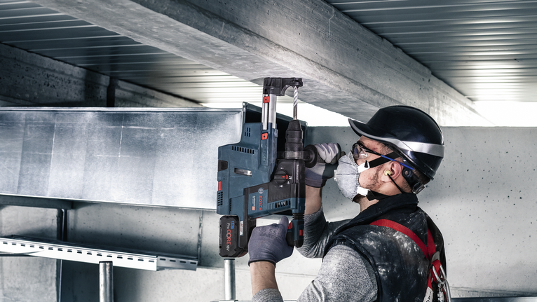 一名佩戴安全设备的人员在建筑工地上钻入金属梁。