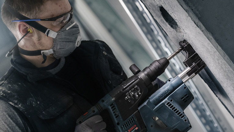 一名佩戴安全设备的人员使用电动工具在混凝土墙上钻孔。