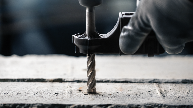 佩戴安全设备的人员使用钻头在混凝土上钻孔。