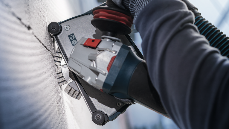 佩戴安全设备的人员使用电动工具磨削墙壁。