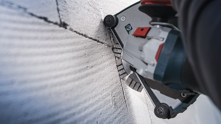 佩戴安全设备的人员使用电动工具在混凝土上切割出直槽。