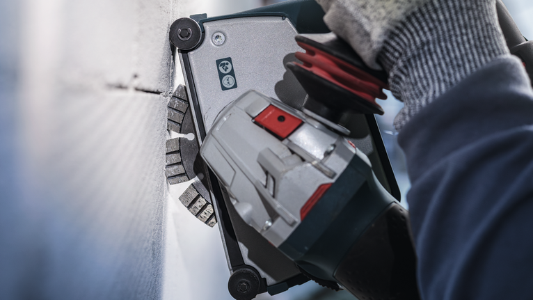 佩戴安全设备的人员使用电动工具切割墙壁。