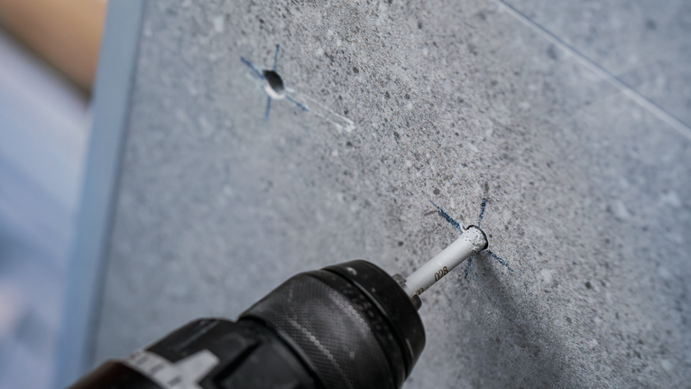 钻头在灰色瓷砖表面上钻出一个精确的孔。