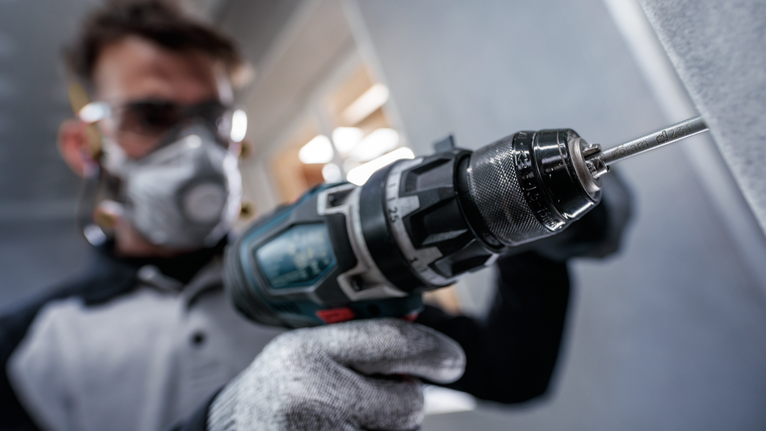 佩戴安全设备的人员使用电动工具在墙上钻孔。