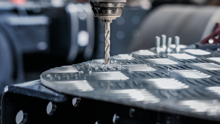 钻头在有纹理的金属板上钻孔。