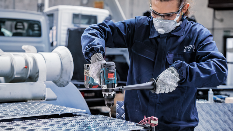 佩戴安全设备的人员在工业环境中钻入金属表面。