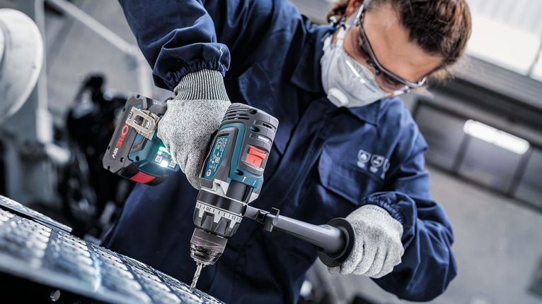 佩戴安全设备的人员使用电动工具钻入金属。